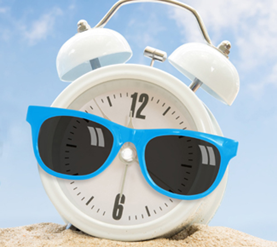 White clock in the sand with blue sun glasses on.