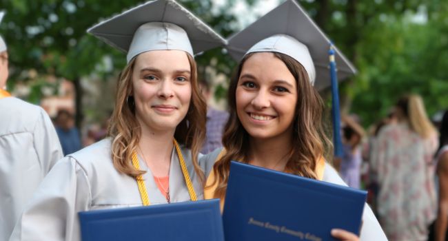 Two students in graduation regalia stand with their diplomas after SCCC's Commencement Ceremony
