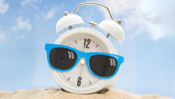 White clock in the sand with blue sun glasses on.