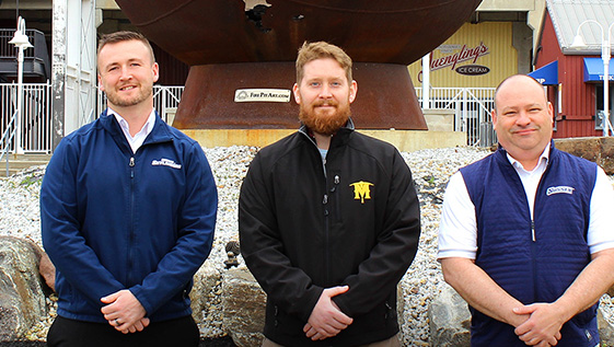Three men stand in front of a stadium.